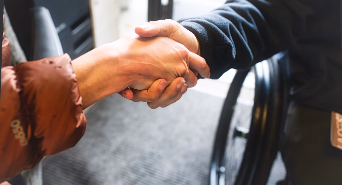 Two people shake hands, one of them a wheelchair user.